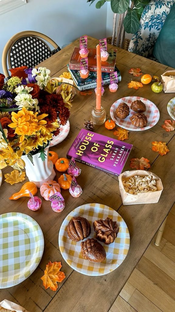 A book sits on a table surrounded by themed decorations and snacks for a book club meeting.