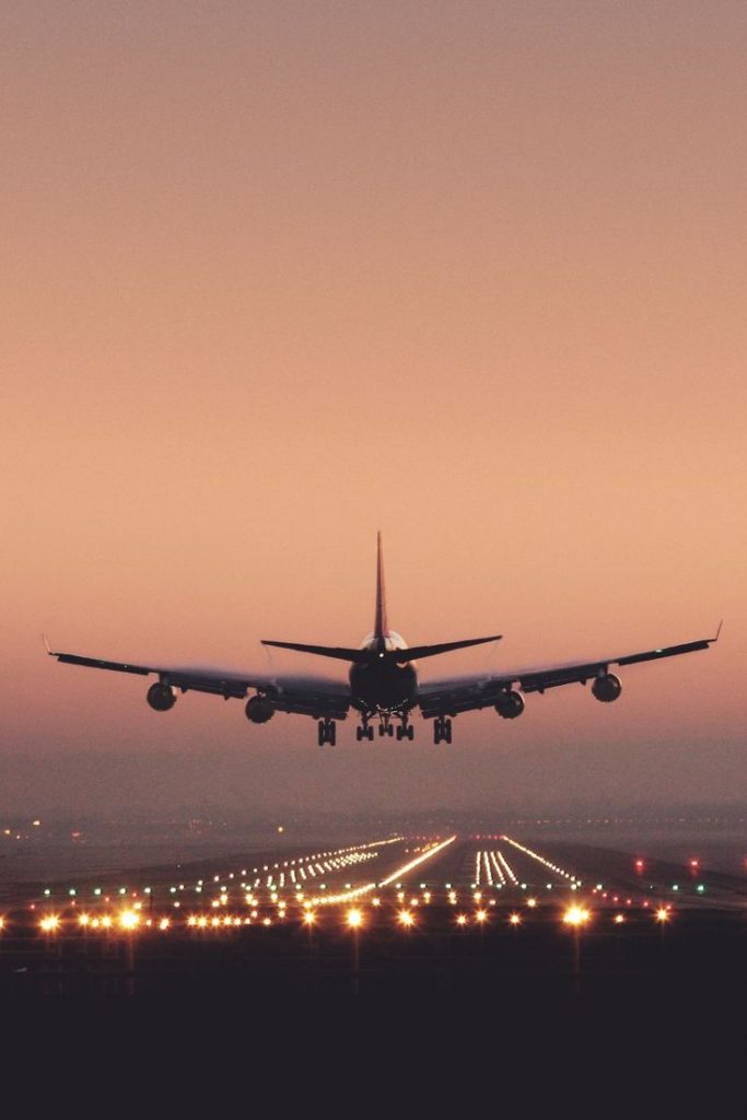 A commercial passenger airplane taking off at sunset, with the aircraft silhouetted against a warm orange sky.