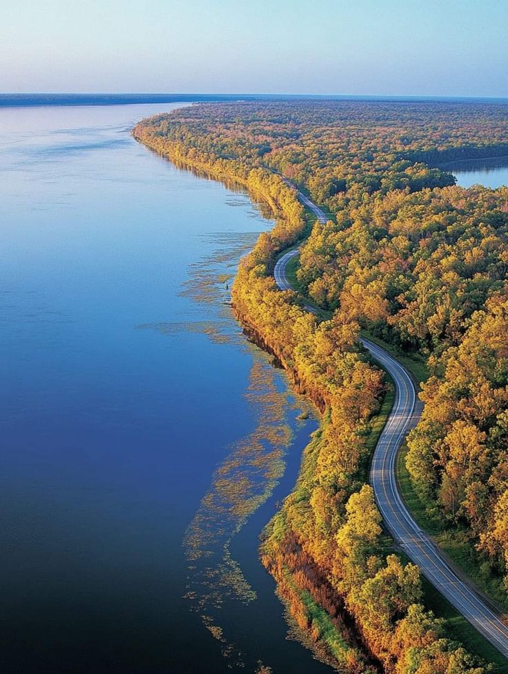 A scenic stretch of the Great River Road running along the Mississippi River, winding through dense forest foliage.