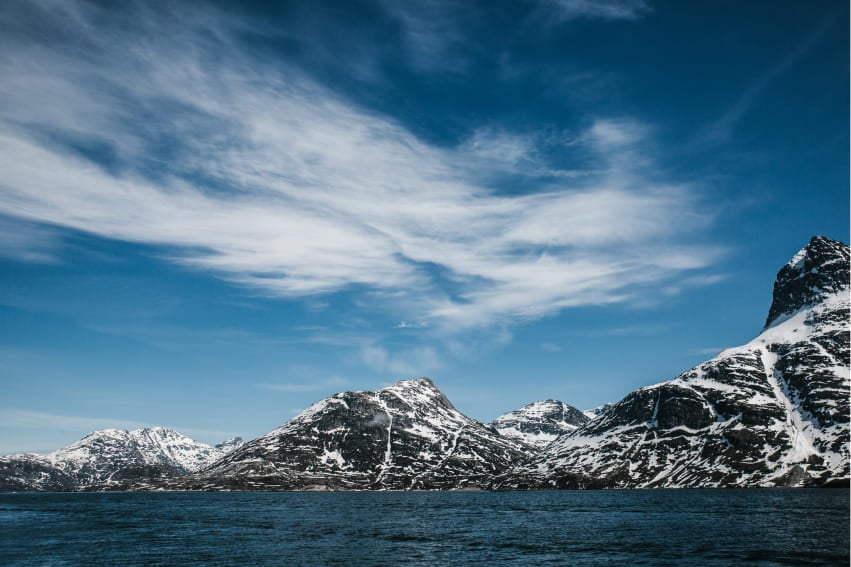 The Lofoten Islands in Nuuk, Norway, featuring jagged mountain peaks covered in snow alongside a deep blue waterway.
